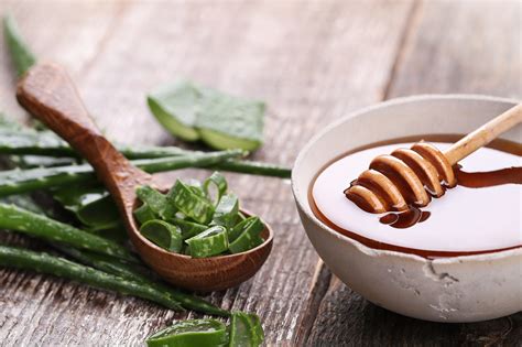 Miska s medom a drevená lyžička, vedľa sú listy aloe vera